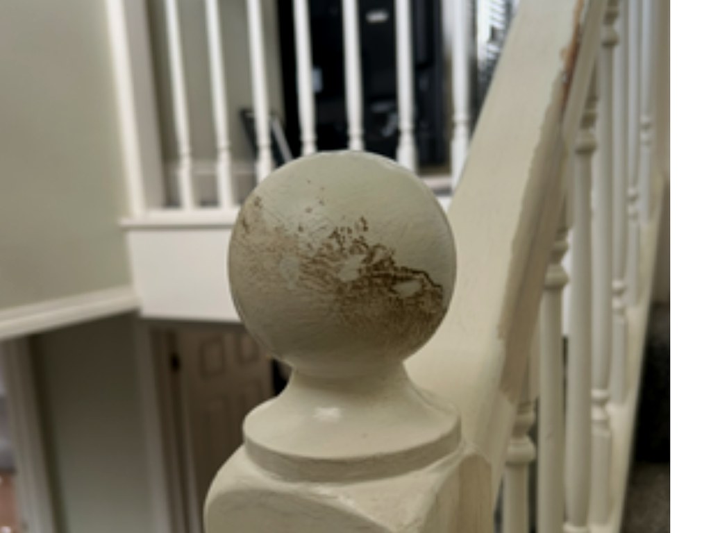 Worn staircase newel post and handrail with flaking paint before preparation