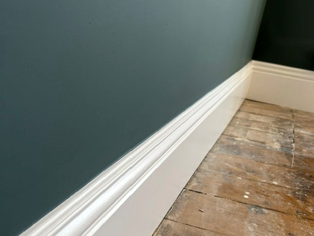 Crisp white moulded skirting board against a deep teal painted wall