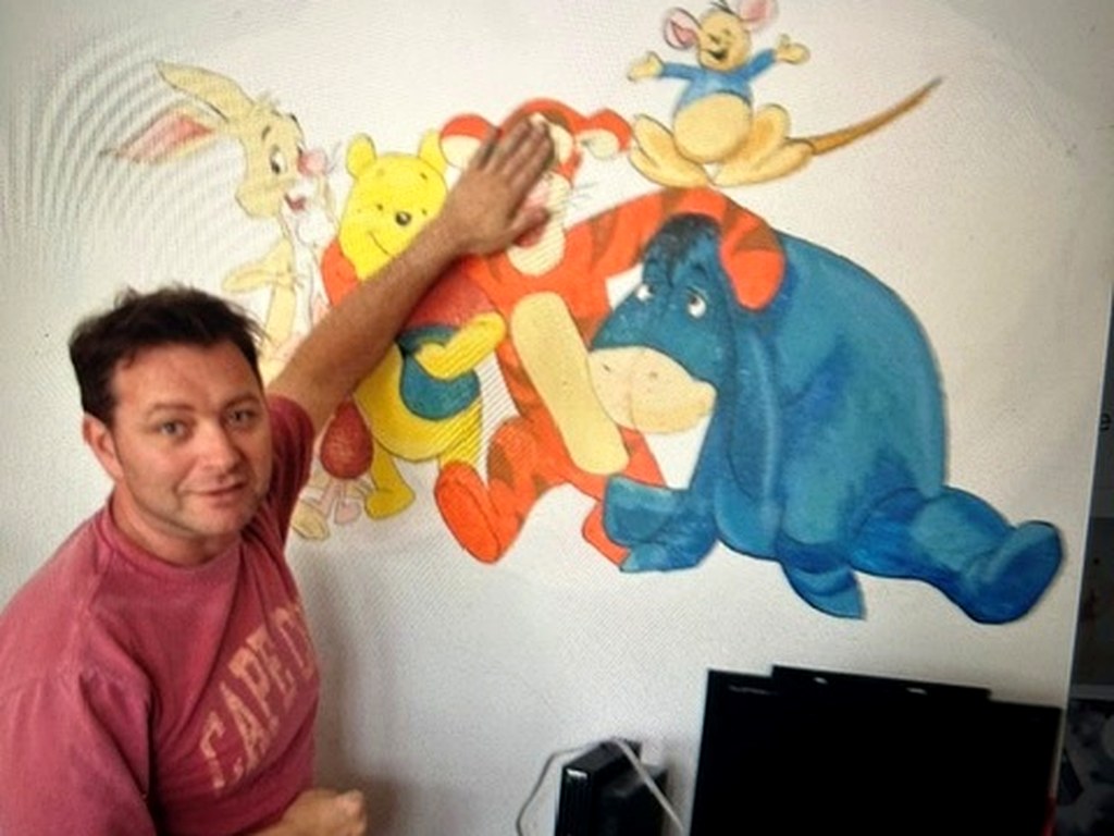 John beside a hand painted Winnie the Pooh and friends mural