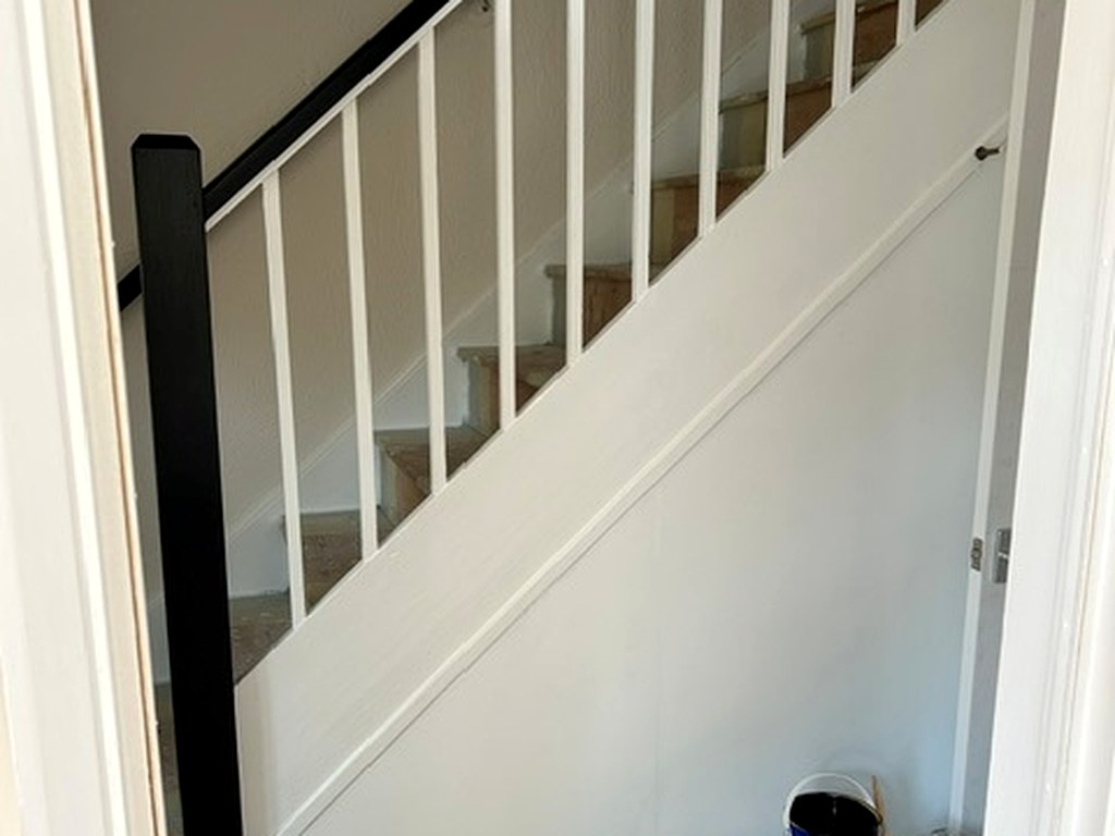Staircase balustrade repainted white with a black handrail and filled, smooth panelling