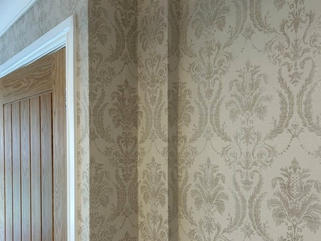 Cream and gold damask wallpaper neatly hung around a hallway doorway and coving
