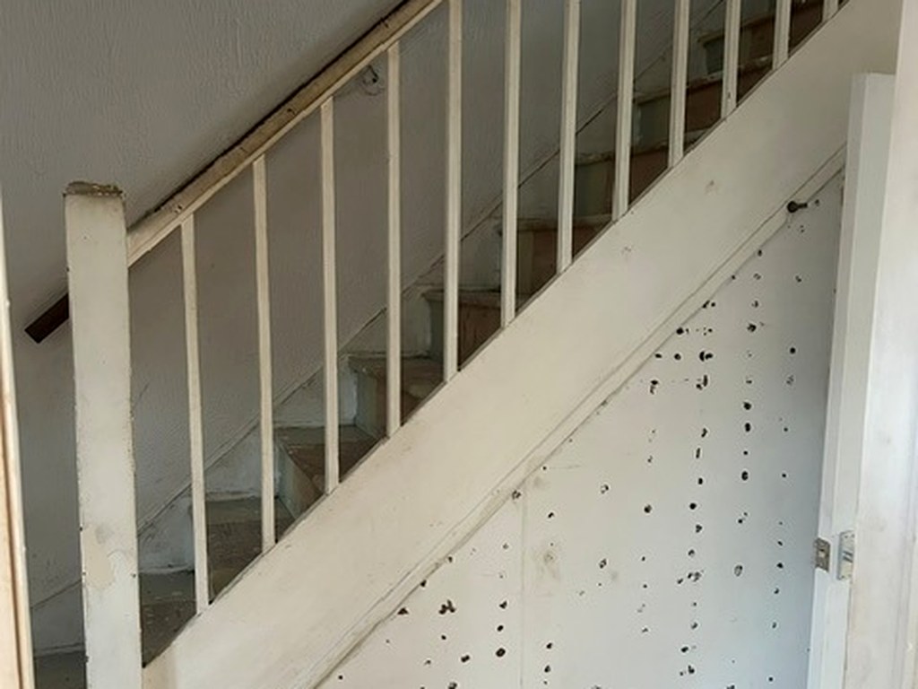 Old staircase balustrade and understairs panelling with damaged, pitted paintwork