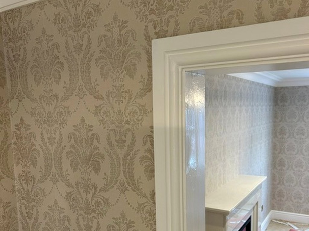 Gold damask wallpaper hung to a crisp edge beside a white painted doorway